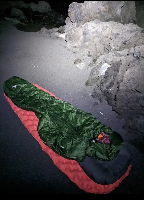 Man sieht die Isomatte am Strand mit einem Schlafsack drauf.