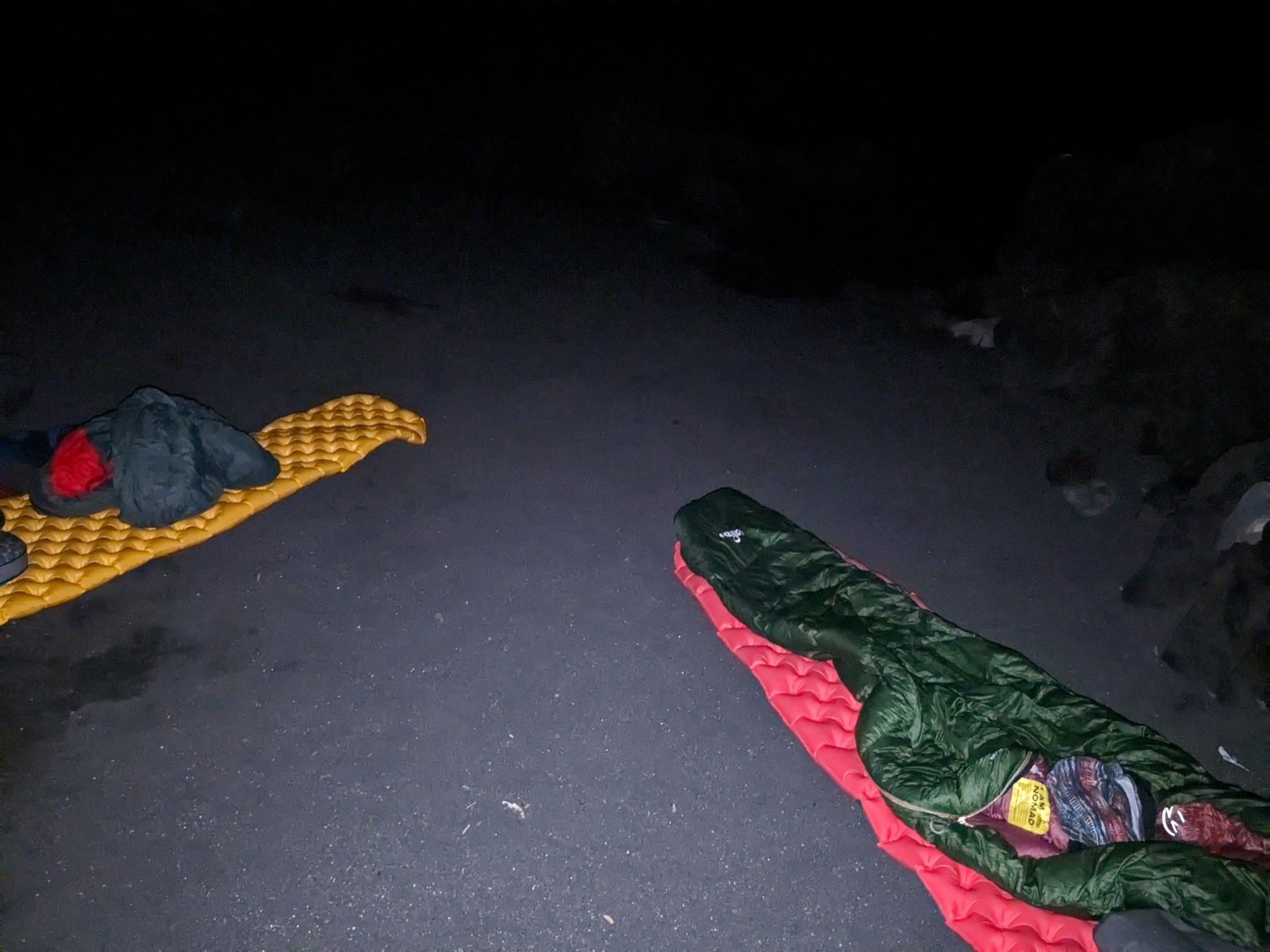 Der Schlafsack liegt auf einer Isomatte am Strand im Dunkeln 