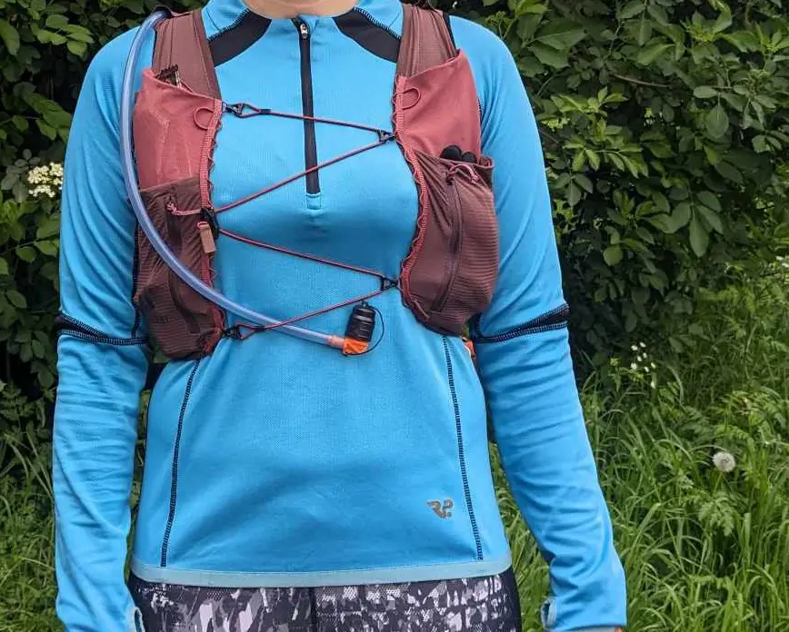 Man sieht die Weste von vorne mit festgeklemmtem Trinkschlauch und Ausrüstung in den Taschen 